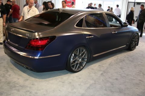 1998 Ford Crown Victoria - same matte dark blue full-size luxury sedan shown from the rear quarter, with chrome trim and dark wheels on a show floor.