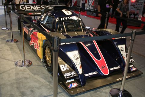 1998 Ford Crown Victoria - dark Red Bull-liveried Hyundai Genesis prototype race car, number 6, displayed front-on behind stanchions at an indoor show.