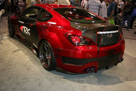 1998 Ford Crown Victoria - candy-red Hyundai coupe with ARK Performance widebody kit, carbon trunk and dual exhausts, shown rear-quarter at an indoor show.
