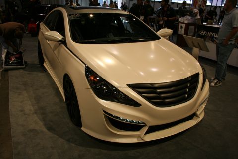 1998 Ford Crown Victoria - pearl-white Hyundai Sonata with custom body kit and LED foglights sits front-quarter on a show floor near a Hyundai booth.