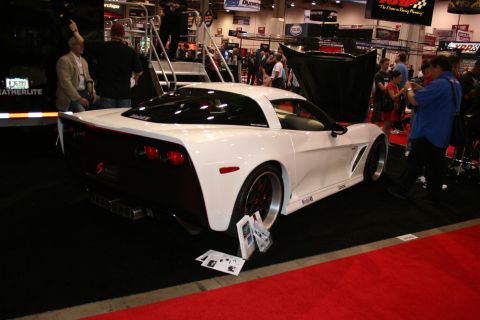 1998 Ford Crown Victoria - white C6-style Corvette coupe with widebody fenders and open rear hatch sits on red carpet at an indoor show.
