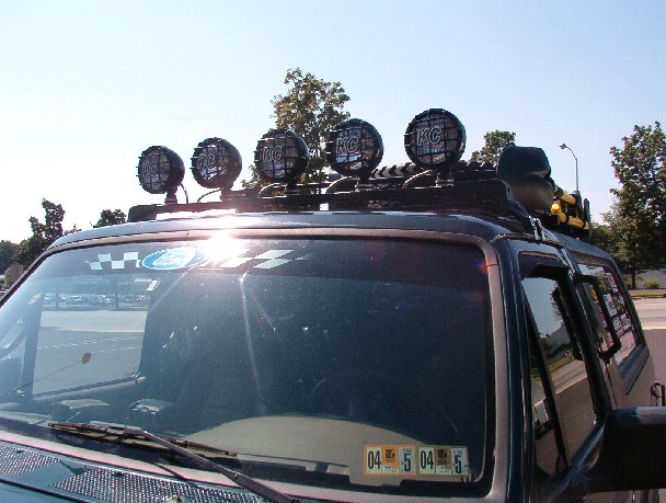 Roof-mounted row of five KC round driving lights on a dark SUV, sun glare on windshield
