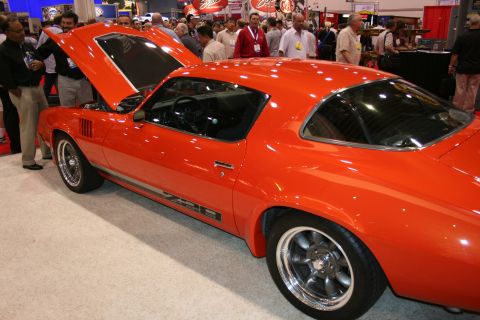 1998 Ford Crown Victoria - orange second-generation Camaro Z28 coupe with raised hood, shown in profile among onlookers at an indoor show.
