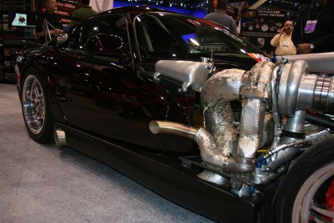 1998 Ford Crown Victoria - black sports car displayed with an exposed turbocharger, heat-wrapped manifold and chrome wheels on a show floor.