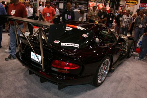 1998 Ford Crown Victoria - black Dodge Viper coupe with large carbon rear wing and rear diffuser, shown rear-quarter amid show crowds.