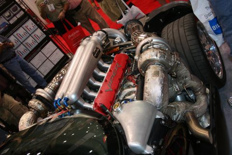 1998 Ford Crown Victoria - exposed twin-turbo V10 engine with red Viper-script cover, polished intake runners and heat-wrapped turbos at an indoor show.