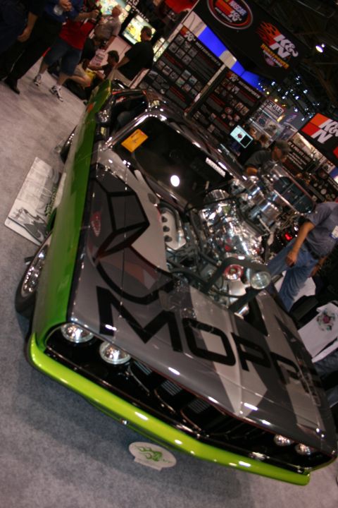 1998 Ford Crown Victoria - custom car painted silver with bold MOPAR lettering and lime-green fenders sits on display amid show booths.