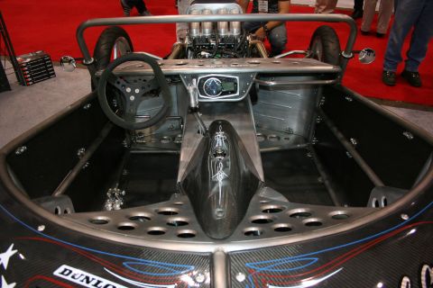 1998 Ford Crown Victoria - stripped open cockpit of a bare-metal custom roadster shows a small steering wheel, single gauge and an exposed engine behind the roll bar.