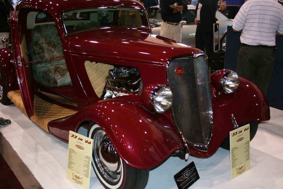 Front three-quarter of a maroon vintage coupe hot rod with chrome headlights and spec cards reading 33 in 66