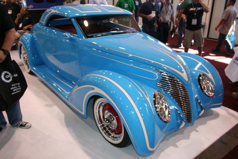 1998 Ford Crown Victoria - sky-blue custom coupe with white pinstriping, chrome grille and red-accented wheels sits on display at an indoor show.