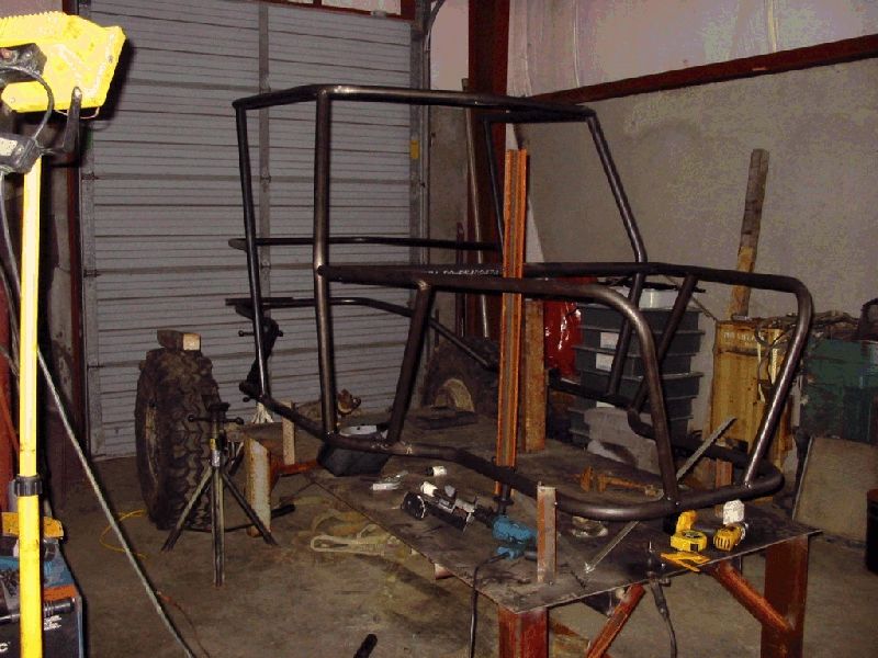 Bare steel tube-frame chassis and roll cage on a welding table in a fab shop