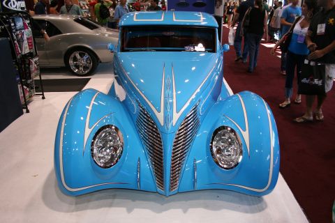 1998 Ford Crown Victoria - head-on front of a sky-blue custom coupe shows a V-shaped chrome grille, twin headlights and flowing white pinstripes.