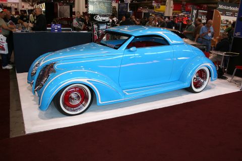 1998 Ford Crown Victoria - sky-blue custom coupe with white pinstriping and red wide-whitewall wheels sits in profile on a show stand.