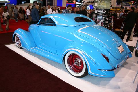 1998 Ford Crown Victoria - rear quarter of a sky-blue custom coupe with white pinstriping and red-spoke whitewall wheels at an indoor show.