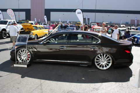 1998 Ford Crown Victoria - lowered dark Lexus luxury sedan rides on large polished multi-spoke wheels in profile at an outdoor car show.