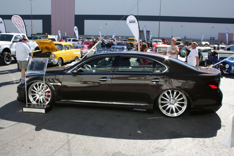 Profile of a lowered dark Lexus luxury sedan on large polished multi-spoke wheels at an outdoor show