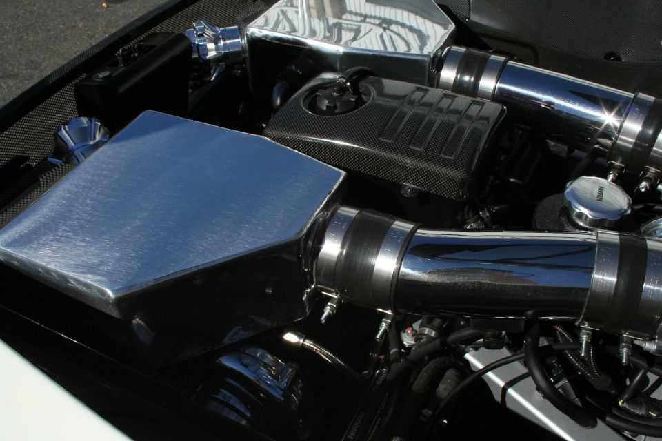 Engine bay close-up showing a polished intake box, carbon-fiber cover and chrome piping