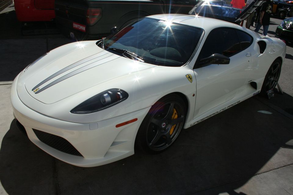 Front three-quarter of a white Ferrari coupe with silver hood stripe and black wheels in sunlit lot
