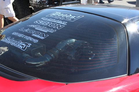 1998 Ford Crown Victoria - rear hatch glass of a red sports car is plastered with sponsor and tuning-brand vinyl decals at an outdoor event.