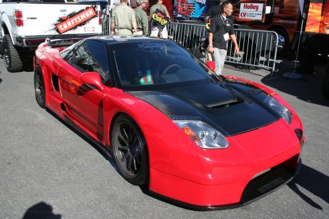 1998 Ford Crown Victoria - modified red two-seat mid-engine sports car with a black hood, widebody kit and black wheels on display at an indoor automotive show.