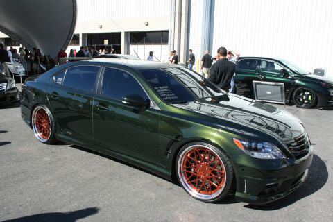 1998 Ford Crown Victoria - slammed dark green full-size luxury sedan sits on large copper-finished multi-spoke wheels inside an exhibition hall.