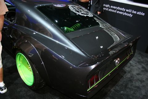 1998 Ford Crown Victoria - rear three-quarter of a dark custom fastback muscle car with widebody fenders and bright green wheels at an indoor show.