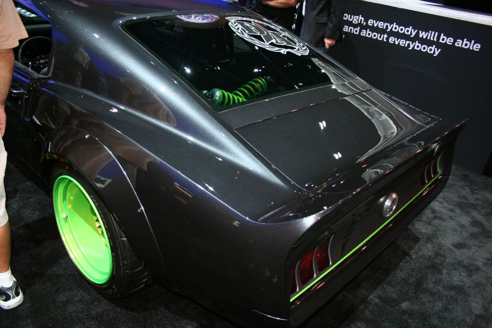 Rear of dark custom fastback muscle car with neon-green wheels indoors