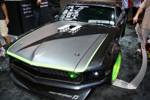1998 Ford Crown Victoria - front of a dark custom Ford Mustang fastback with green-edged graphics, a hood scoop and green-tinted headlights at a show.