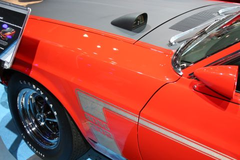1998 Ford Crown Victoria - Close-up of an orange Ford Mustang's front fender showing a Boss 302 side stripe, hood scoop and chrome wheel.