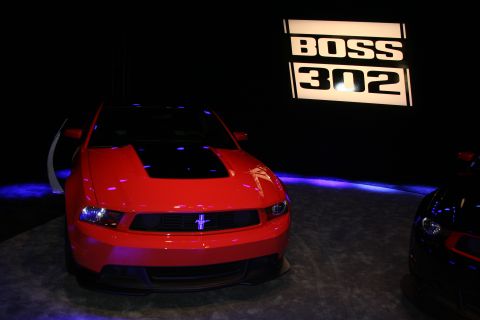 1998 Ford Crown Victoria - red Ford Mustang coupe sits on a dark stage with purple lighting next to an illuminated Boss 302 backdrop sign.