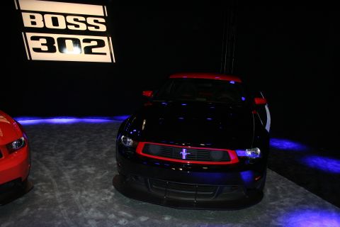 1998 Ford Crown Victoria - black Ford Mustang coupe with a red grille accent sits on a dark stage beside a glowing Boss 302 backdrop sign.