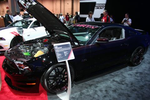 1998 Ford Crown Victoria - black Ford Mustang coupe sits with its hood open exposing the engine bay, displayed on red carpet at an indoor show.