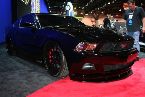 1998 Ford Crown Victoria - glossy black Ford Mustang coupe with red-accented black wheels sits on red carpet at an indoor automotive show.