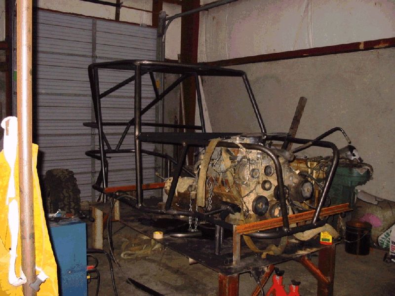 Bare tube chassis on a fab table with V8 and transmission mocked up in a shop