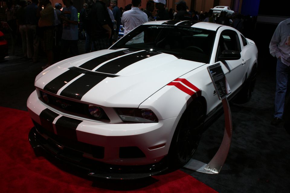 White Mustang coupe with black and red racing stripes on red carpet