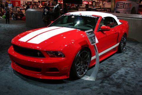 1998 Ford Crown Victoria - red Ford Mustang convertible with a white folding top and white center stripes sits on display at an indoor automotive show.