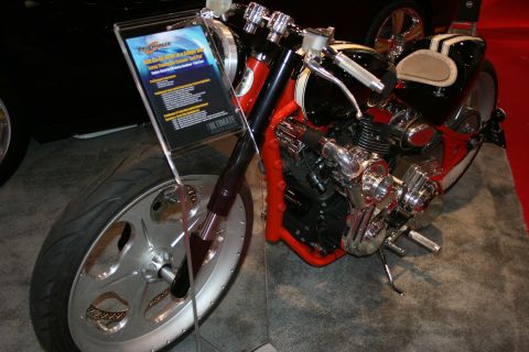 1998 Ford Crown Victoria - custom chopper motorcycle with a chromed V-twin engine, solo seat and disc front wheel displayed beside an info placard.