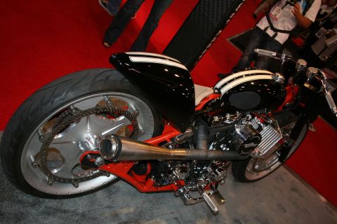 1998 Ford Crown Victoria - Rear three-quarter view of a black custom chopper with red frame, exposed chain drive and fat rear tire on a red floor.