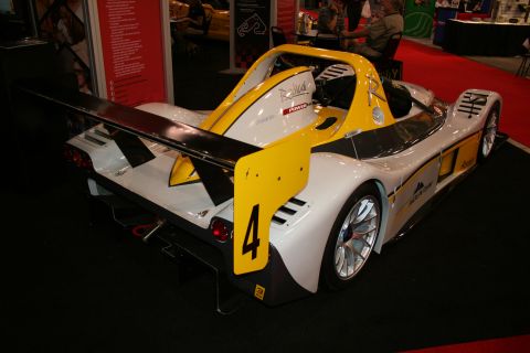 1998 Ford Crown Victoria - Rear view of a white and yellow open-cockpit track car numbered 4 with a large rear wing on an auto show stand.