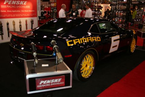 1998 Ford Crown Victoria - black Chevrolet Camaro with yellow CAMARO graphics and yellow wheels displayed at a Penske Racing Shocks booth.