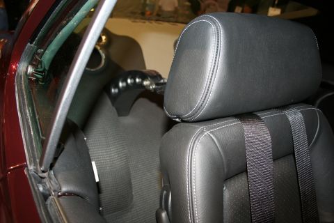 1998 Ford Crown Victoria - Close-up of a black leather bucket seat headrest and seatbelt webbing inside a car with maroon interior trim.