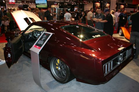 1998 Ford Crown Victoria - Rear three-quarter view of a dark maroon custom fastback muscle car with open door and info placard on a crowded show floor.