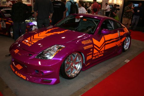 1998 Ford Crown Victoria - purple Nissan 350Z coupe with orange Megan Racing graphics, body kit and silver wheels displayed on a red show floor.