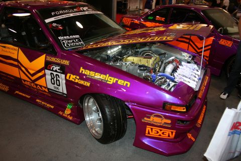 1998 Ford Crown Victoria - purple Formula Drift coupe numbered 86 with orange graphics and open hood exposing a turbocharged engine at a show.