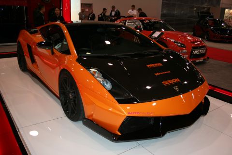 1998 Ford Crown Victoria - orange and black Lamborghini Gallardo with sponsor decals sits on a white display stand at a show.
