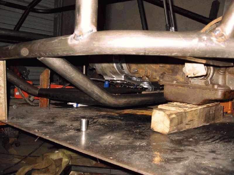 Undercarriage of a vehicle with exposed frame, transmission, and exhaust pipes. Wood blocks support the frame