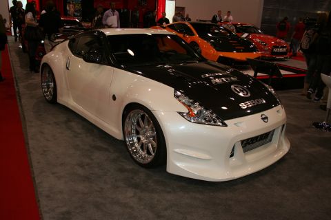 1998 Ford Crown Victoria - widebody white Nissan 370Z with a black hood and chrome wheels displayed on a show floor.