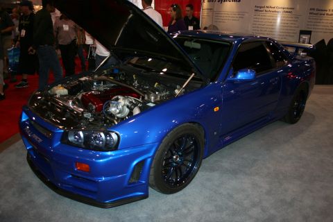 1998 Ford Crown Victoria - Front three-quarter of a blue Nissan Skyline GT-R R34 with raised hood and black wheels on a red carpet.