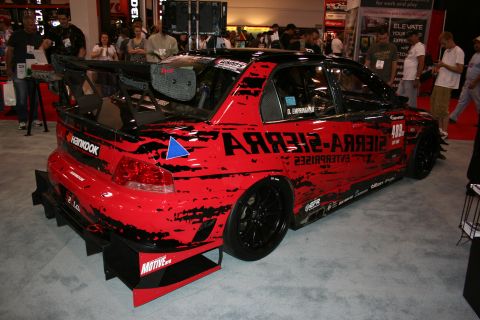 1998 Ford Crown Victoria - red and black race sedan wearing Sierra-Sierra Enterprises livery and a large rear wing on a show floor.