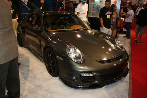 1998 Ford Crown Victoria - dark gray Porsche 911 Turbo with black wheels and a front lip sits on a white display stand at a show.